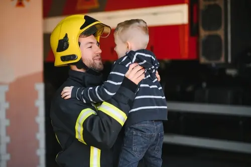 a dad in his firefighter gear lifts his beneficiary son up